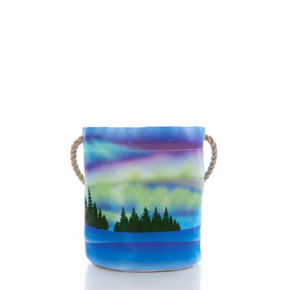 Introducing the Northern Lights Bucket Bag by Sea Bags—a fabric bucket with rope handles, crafted from recycled sail cloth and adorned with a vibrant northern lights design above a silhouette of trees and water. by Sea Bags