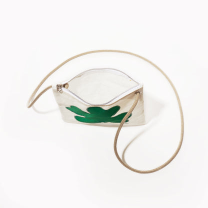 The Sea Bags Four Leaf Clover Slim Crossbody, crafted from durable sail cloth, features a green abstract clover design on the front, a beige shoulder strap, and a compact white zippered silhouette—an ideal handbag alternative—shown on a white background. by Sea Bags