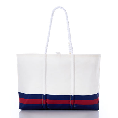Introducing the New York Giants Tailgate Tote by Sea Bags: a white tote bag featuring blue and red horizontal stripes at the bottom and two sturdy white rope handles, displayed on a white background. Crafted from recycled sail cloth, this eco-friendly tote blends nautical style with sustainable design for a fashionable and earth-conscious way to support your team. by Sea Bags