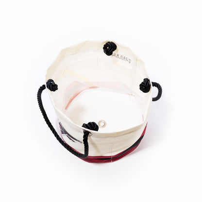 The Atlanta Falcons Beverage Bucket by Sea Bags is a round white and red bucket bag made from recycled sail cloth, featuring black rope handles secured with four black knots and a metal grommet at the base, as seen from above. by Sea Bags