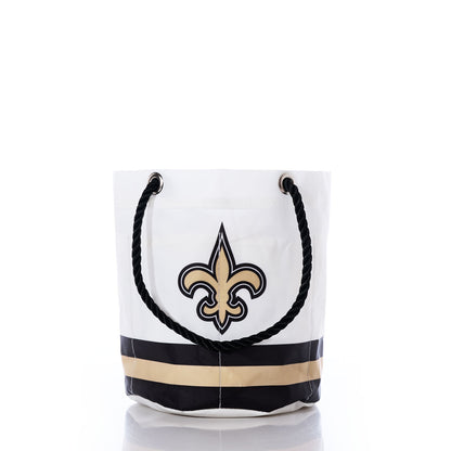 Introducing the New Orleans Saints Beverage Bucket by Sea Bags—a white tote with sturdy black rope handles, adorned with a striking gold and black fleur-de-lis logo and accented by bold horizontal stripes in black and gold at the base. This stylish and sustainable bucket is perfect for any New Orleans Saints fan’s collection or as a chic alternative to a cooler for carrying your favorite beverages and essentials. by Sea Bags