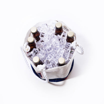 Six brown glass bottles with gold caps are arranged upright in a Sea Bags New York Giants Beverage Bucket, crafted from white sail cloth and filled with ice cubes, viewed from above against a plain white background. by Sea Bags