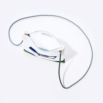 The Sea Bags Seattle Seahawks Slim Crossbody is a small white zippered pouch crafted from recycled sail cloth, featuring a navy and green abstract design reminiscent of a Seahawks bag. It includes a silver zipper and a thin gray cord strap, shown against a white background. by Sea Bags