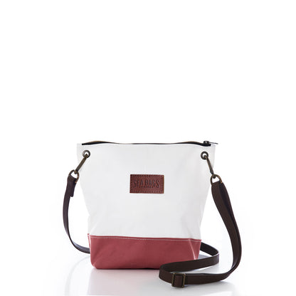 The Sea Bags Nantucket Red Chebeague Crossbody Bag features a two-tone design with a white upper made from recycled sail cloth and a Nantucket Red cotton canvas base. It is accented by a dark adjustable strap and a brown leather Sea Bags patch on the front, all displayed against a plain white background. by Sea Bags