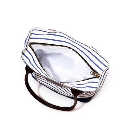 Top view of an open Sea Bags Navy Mariner Stripe Chebeague Handbag, handmade from recycled sail cloth with dark handles and a zippered closure, revealing an empty white-lined interior against a white background. by Sea Bags