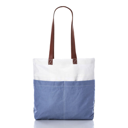 The Sea Bags Chambray Blue Chebeague Market Tote, crafted from recycled sails, showcases a two-tone design with a white upper section, chambray blue lower section, and durable brown leather handles, displayed against a white background. by Sea Bags