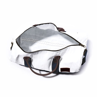 The Chebeague Duffel by Sea Bags is a white duffel bag crafted from recycled sail, featuring premium leather handles and a wide-opening zipper that reveals a spacious, empty interior lined with a distinctive zigzag stitch pattern. by Sea Bags