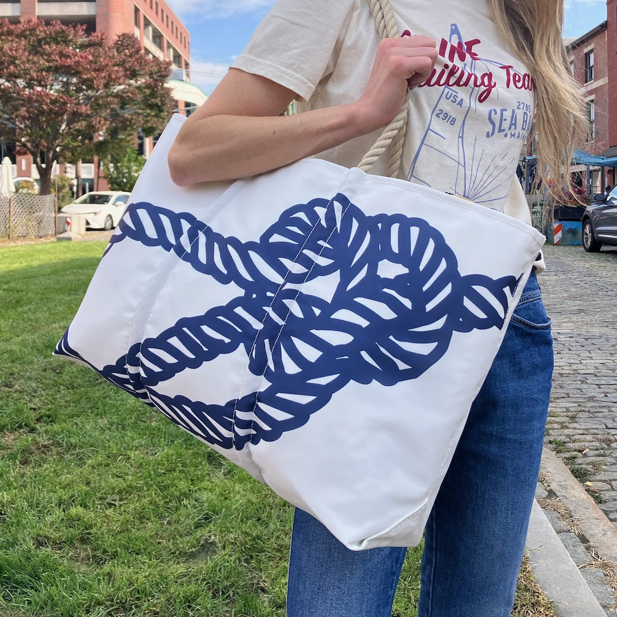 A person holds the Sea Bags Navy Bowline Large Tote, featuring a navy knot design, on a cobblestone street—part of the Anniversary Archive Collection.
