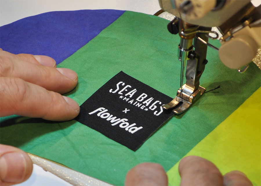 Sea Bags x Flowfold label is being sewn on to the front of the colorful recycled sail cloth backpack