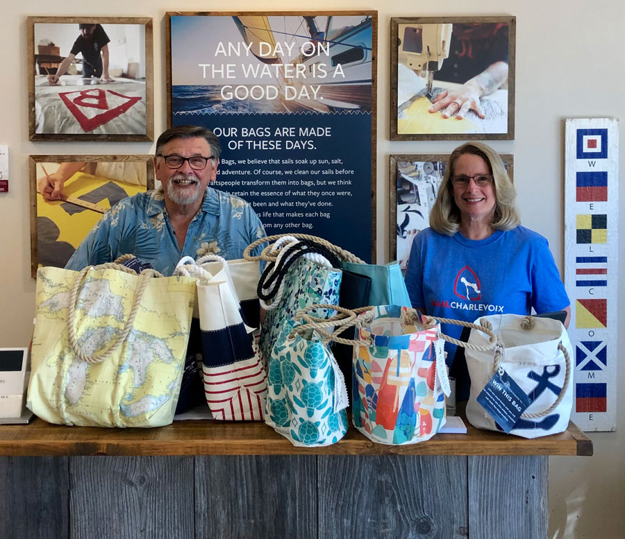 A man and woman stand behind the cash register at the Sea Bags store in Charlevoix, behind a stack of recycled sail cloth totes and accessories.