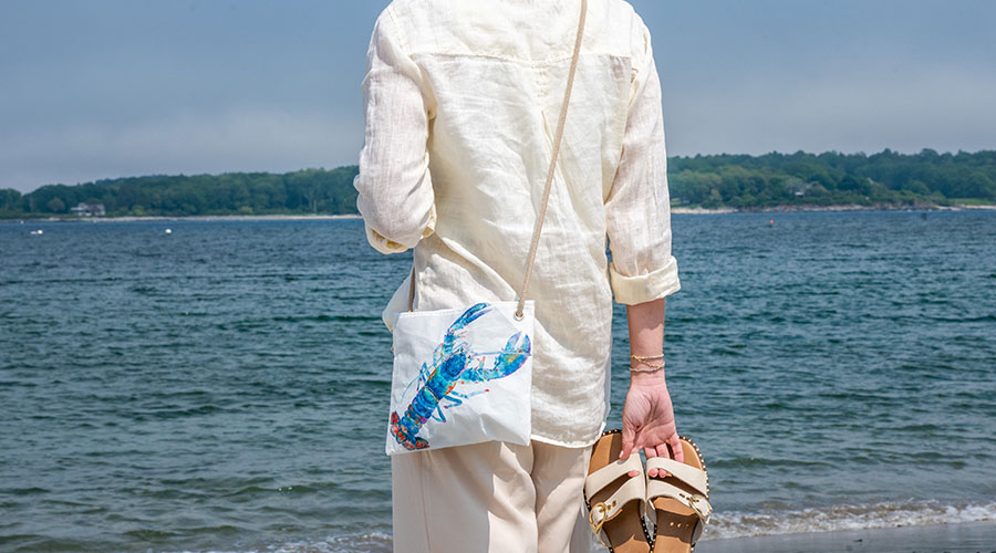 Watercolor Lobster Crossbody worn over the shoulder on a beach