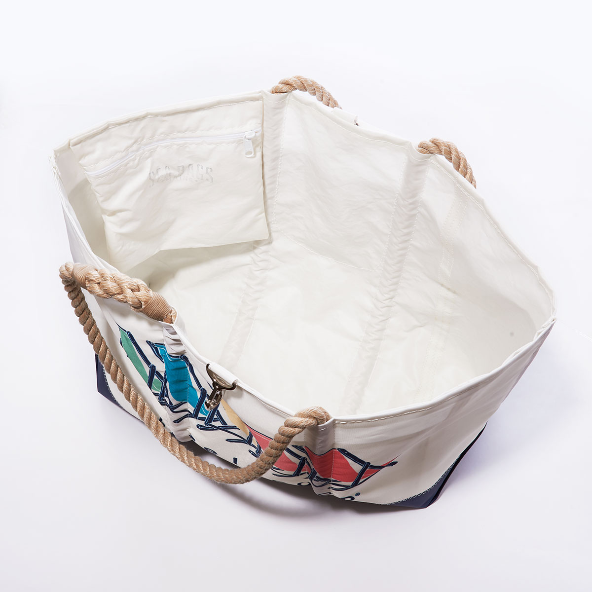 inside view showing hanging interior pocket of a white recycled sail cloth tote with hemp rope handles has a navy bottom and is printed with five beach chairs in red orange yellow green and blue with the life is good brand name under the chairs