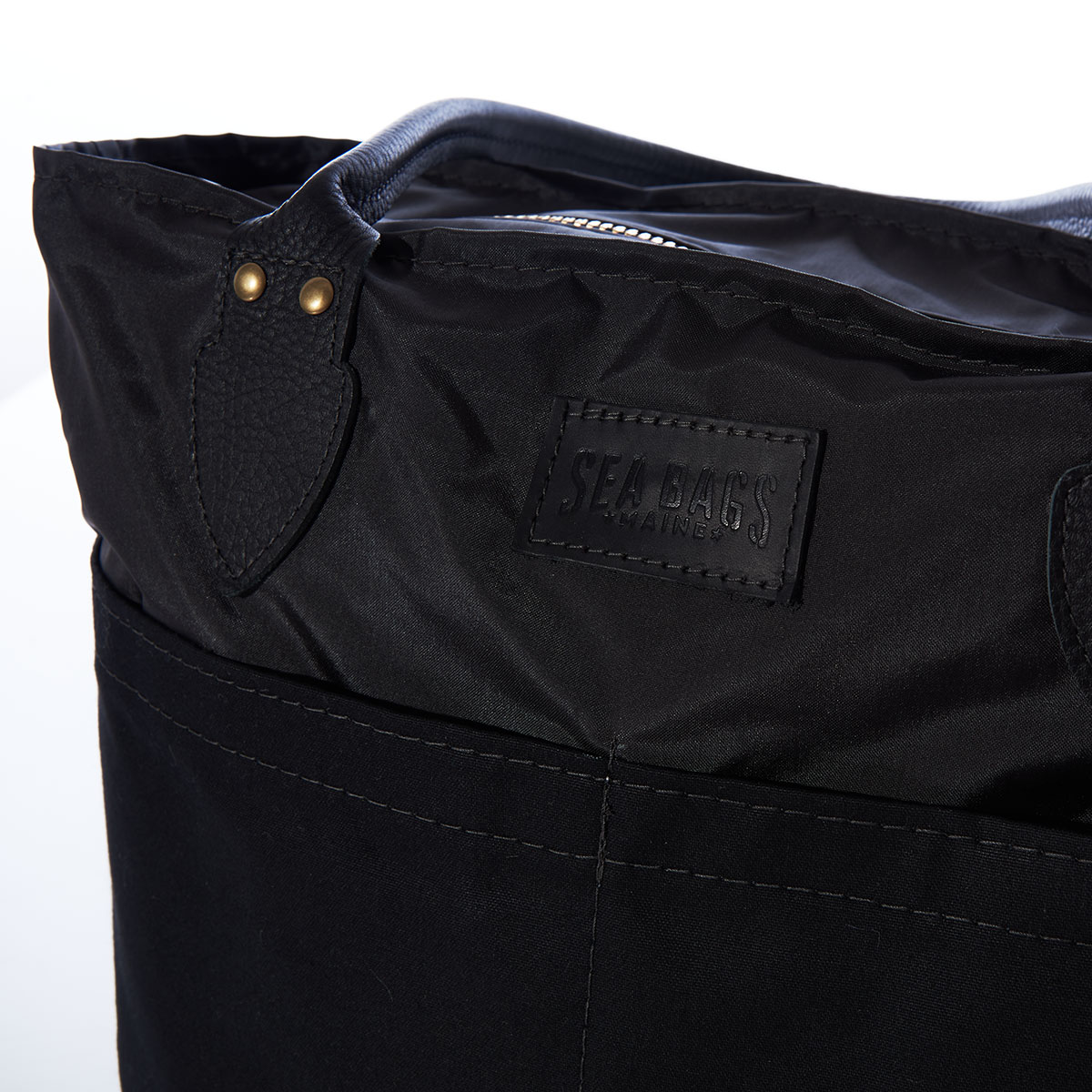 close up view of zipper closure on a black recycled sail cloth medium tote with a black canvas bottom and leather handles