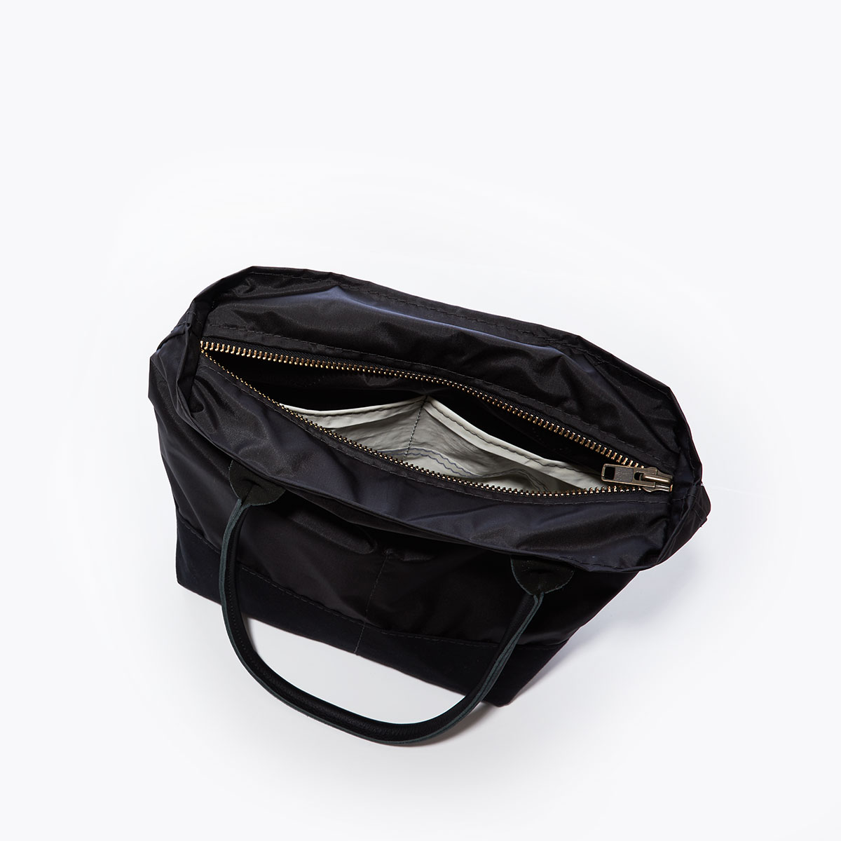 inside view showing interior side pockets of a black recycled sail cloth handbag with a black canvas bottom and leather handles
