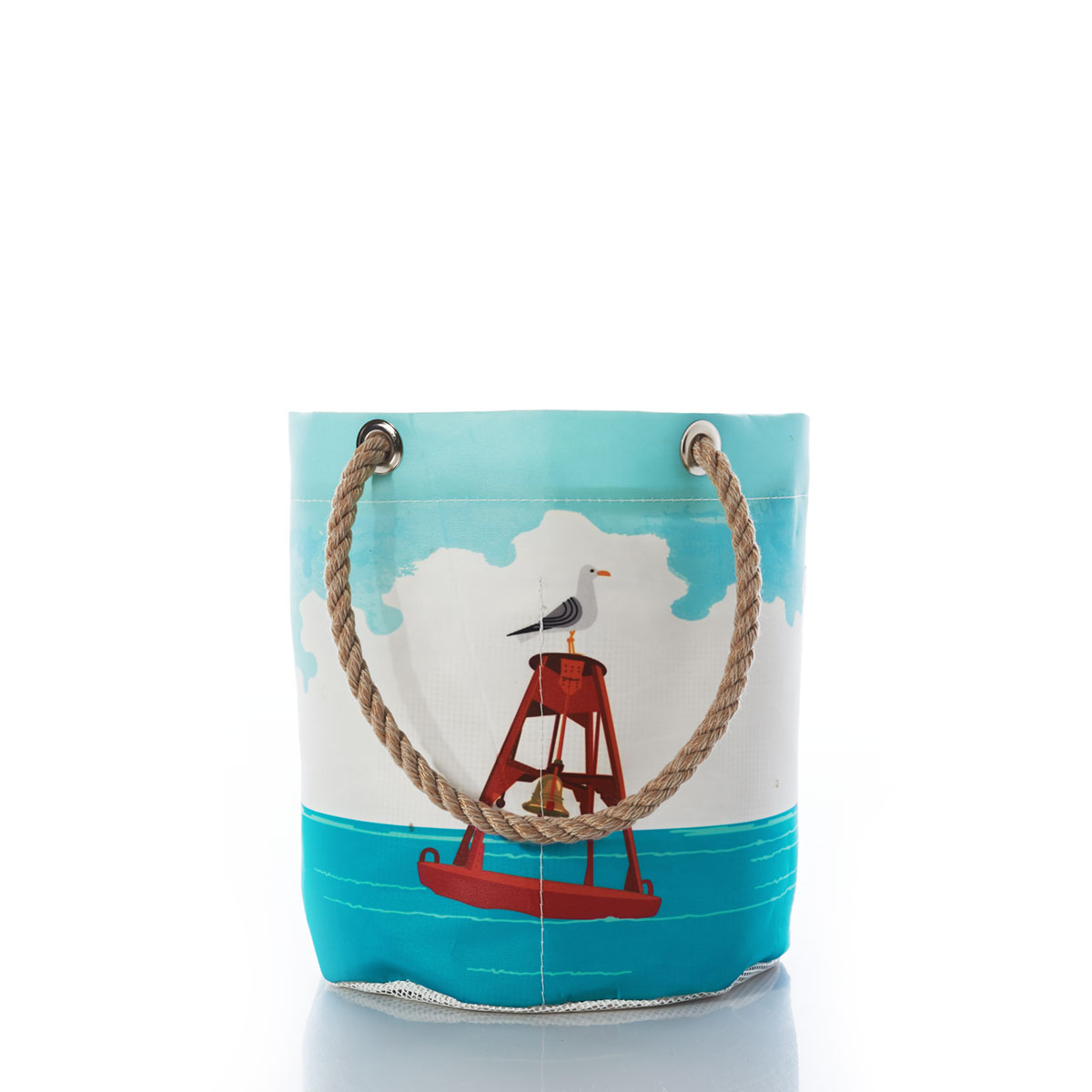 a recycled sail cloth beachcomber bucket with hemp rope handles is printed with an ocean scene and a red bell buoy floats with a seagull perched on top