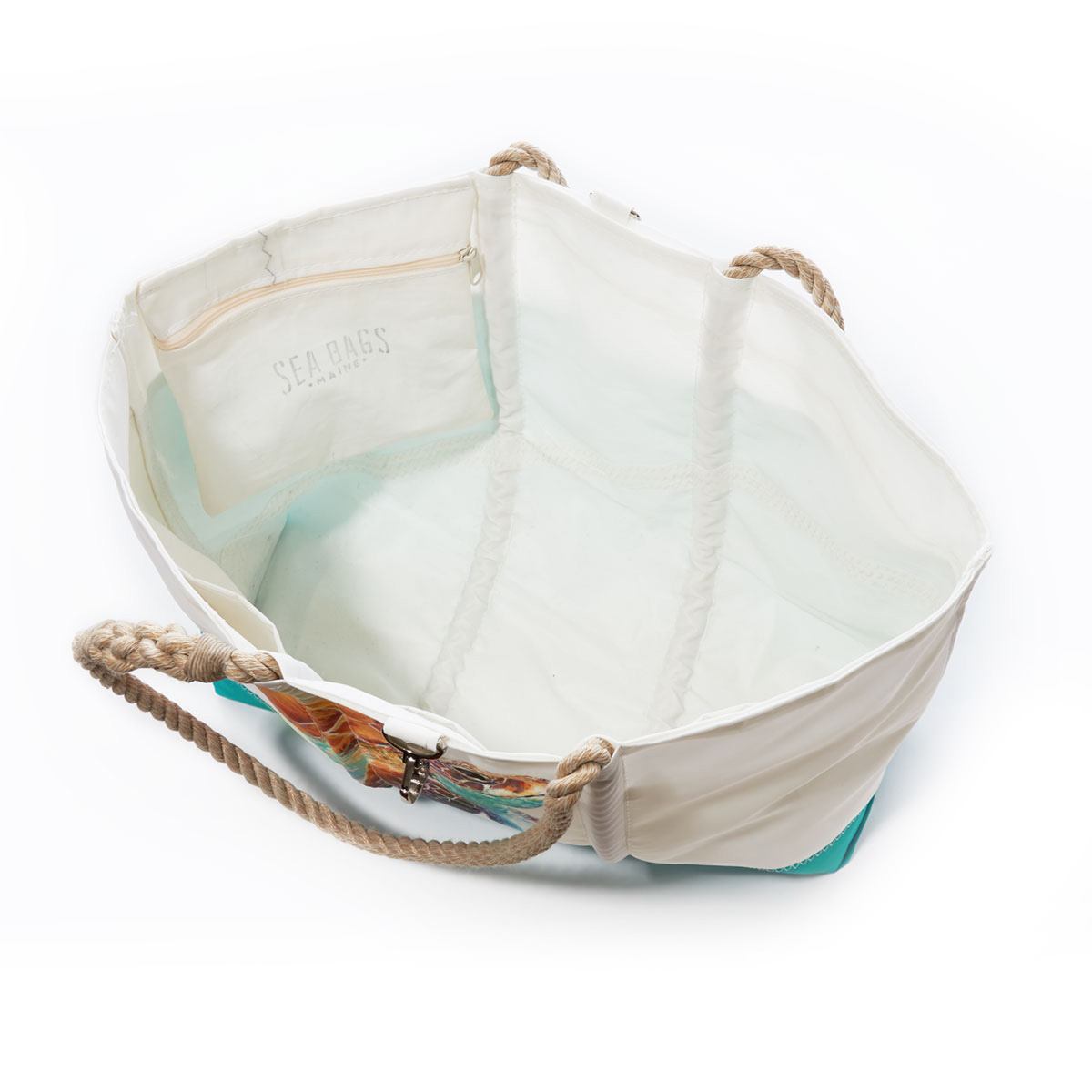 inside view of a white recycled sail cloth beach tote with hemp rope handles and a teal wraparound back pocket is printed with a bright friendly multicolor sea turtle