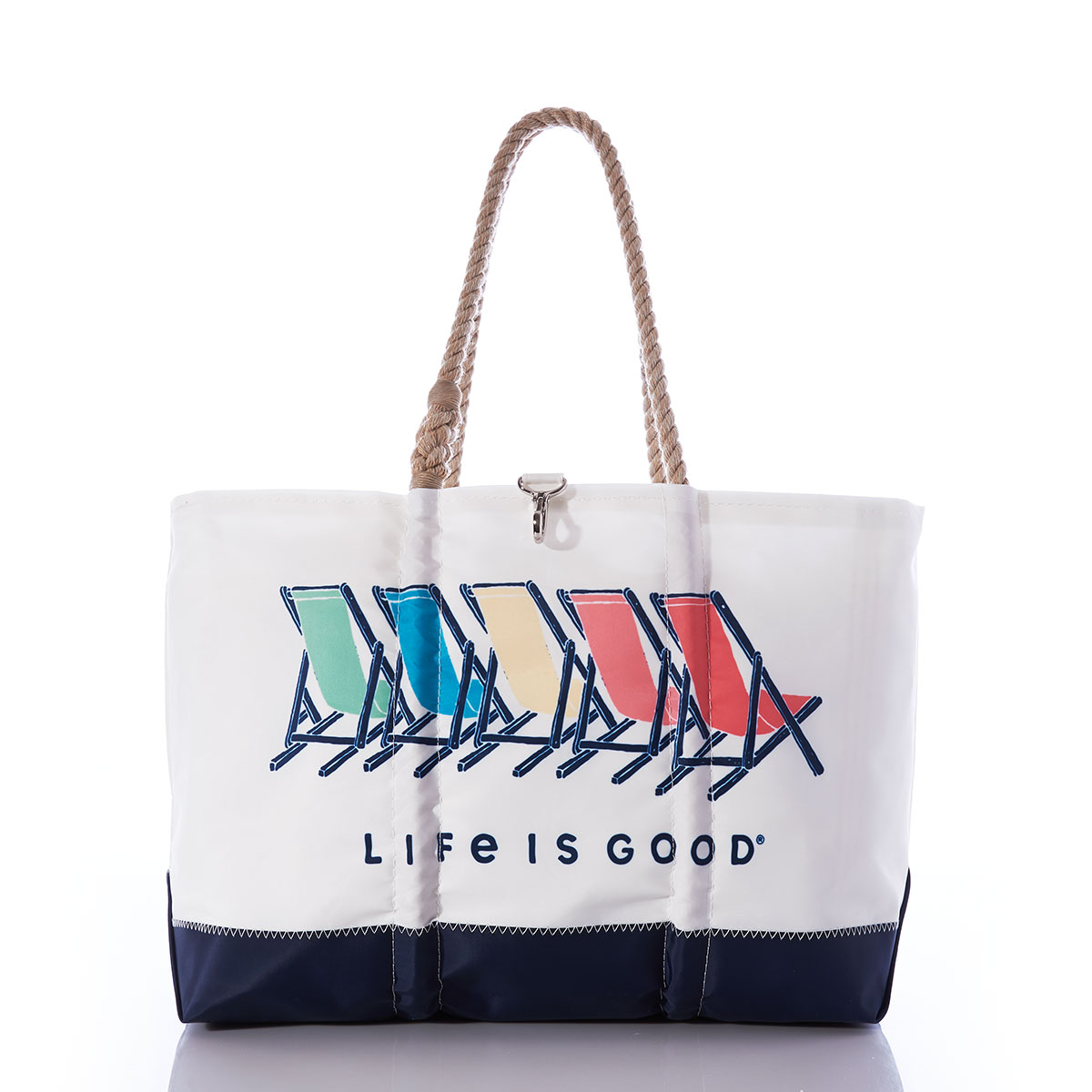a white recycled sail cloth tote with hemp rope handles has a navy bottom and is printed with five beach chairs in red orange yellow green and blue with the life is good brand name under the chairs