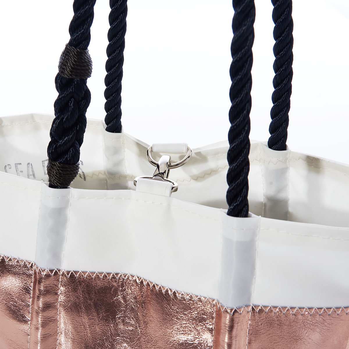 close up of clasp closure of tote with stripes of white, rose gold leather applique, and navy and white sailor stripes on a recycled sail cloth handbag with navy rope handles