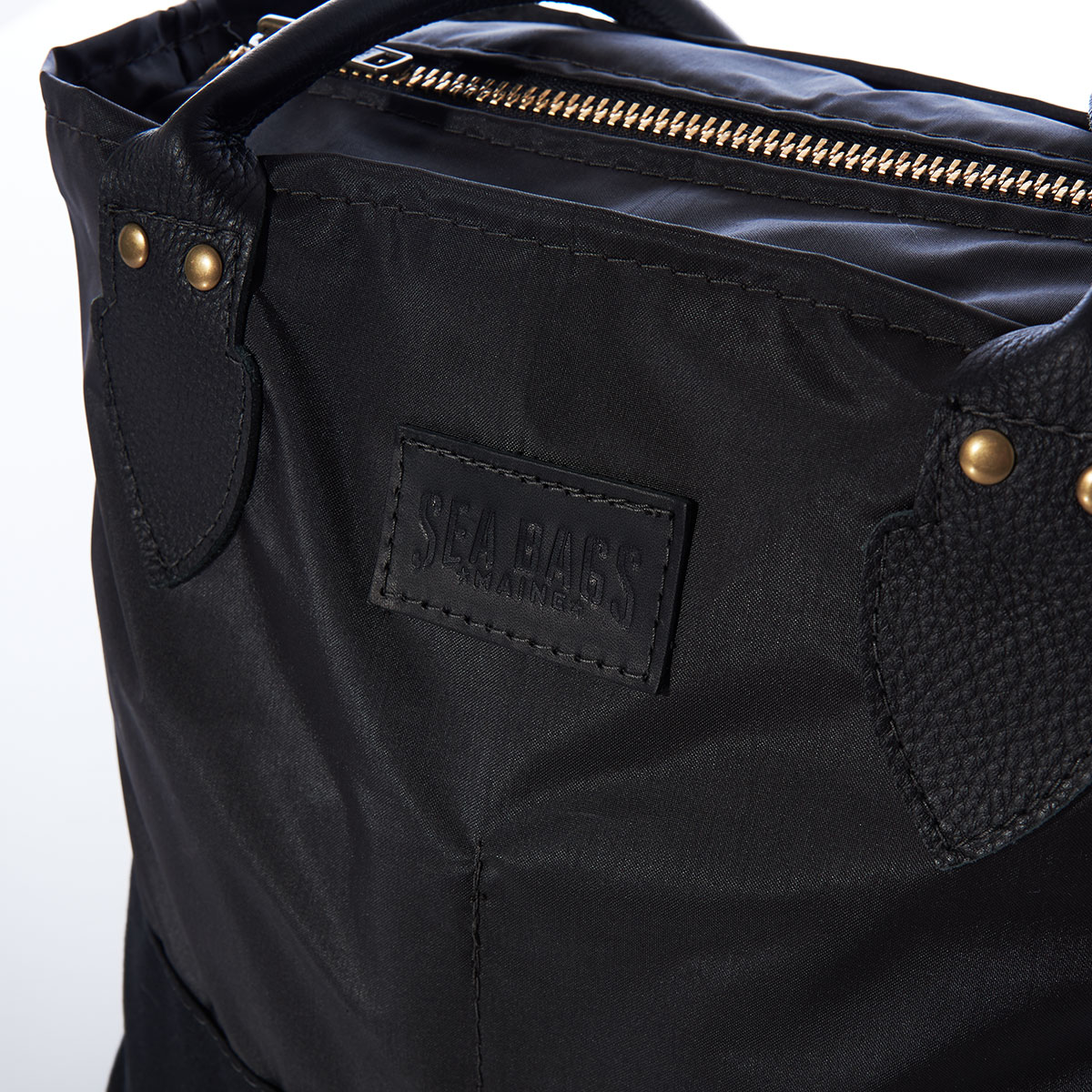 close up view of zipper closure on a black recycled sail cloth handbag with a black canvas bottom and leather handles