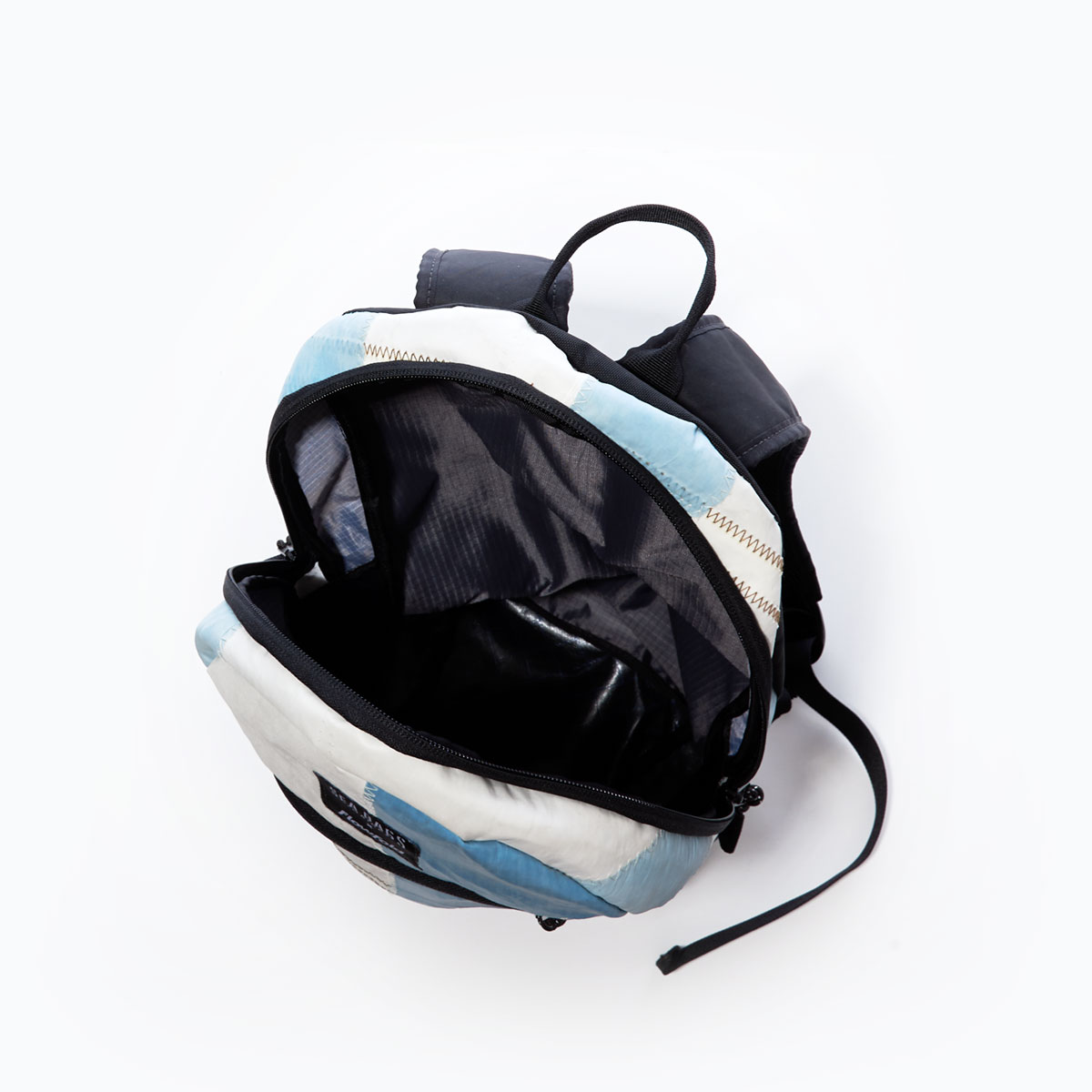 inside view of a backpack with a black canvas base, straps, and front zipper with blue and white recycled sail cloth
