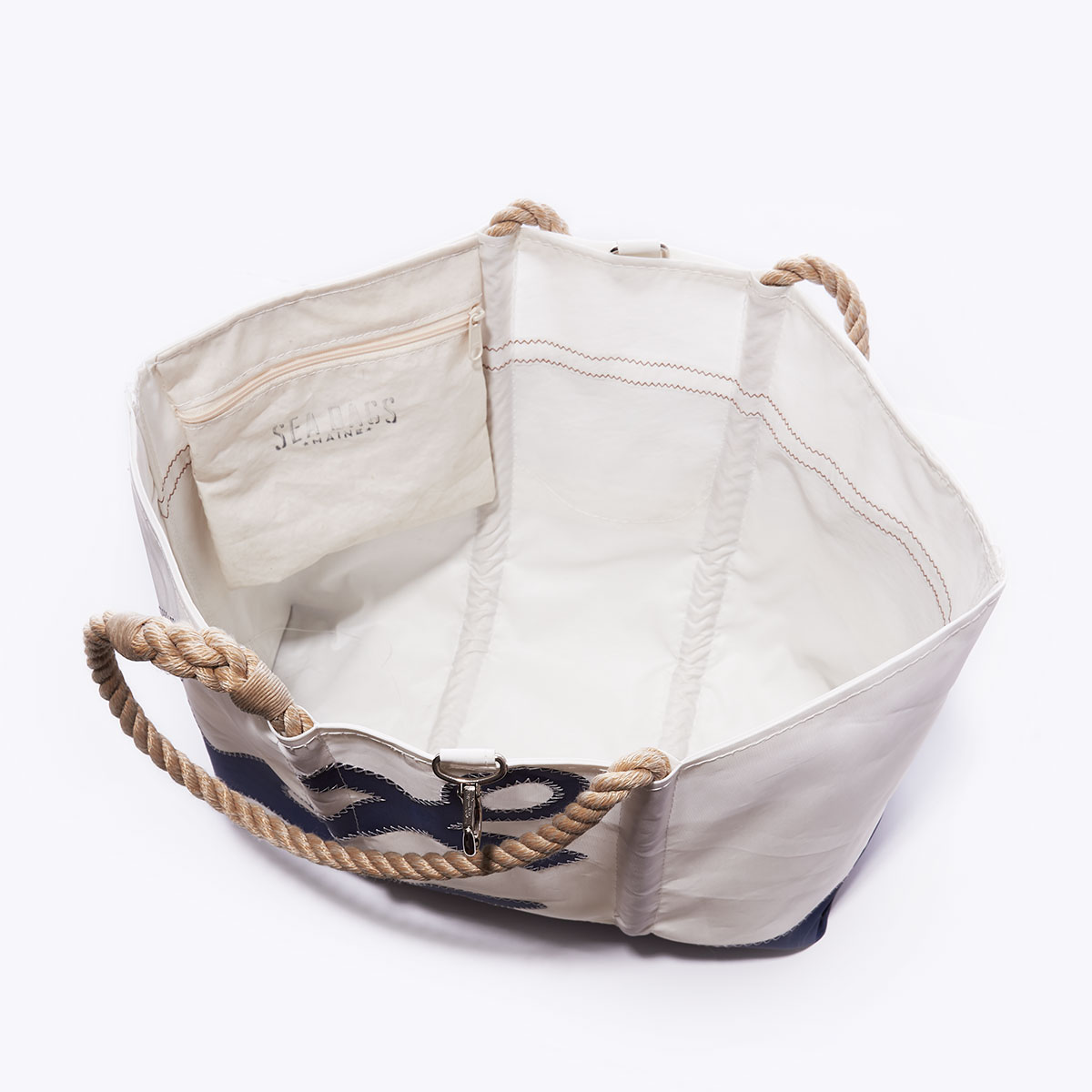 inside view of interior hanging pocket of the beach bag with a navy anchor sits left of center on a white recycled sail cloth tote with a navy bottom and hemp rope handles