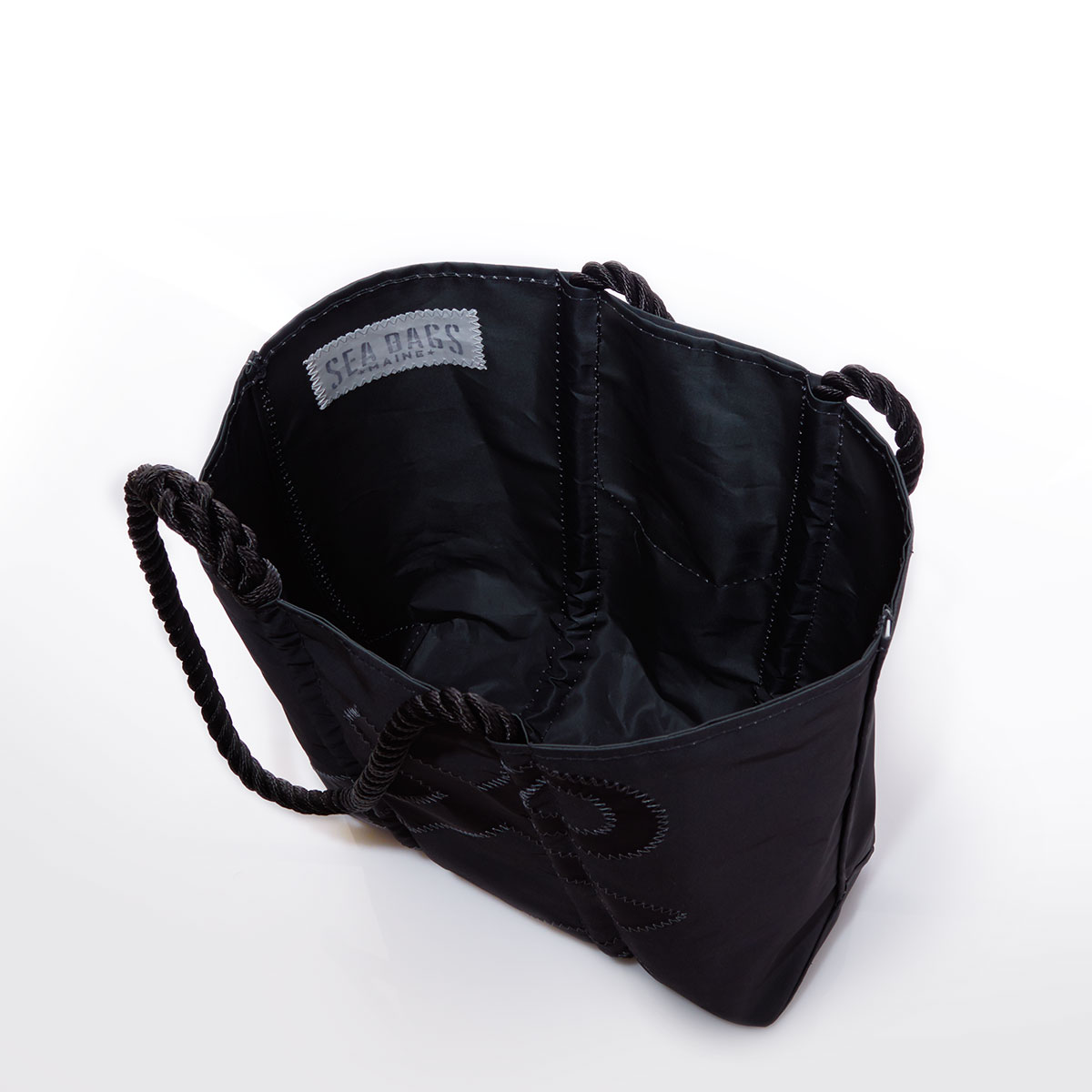 interior view of black recycled sail cloth tote with a black anchor applique and black rope handles and metal top clasp closure