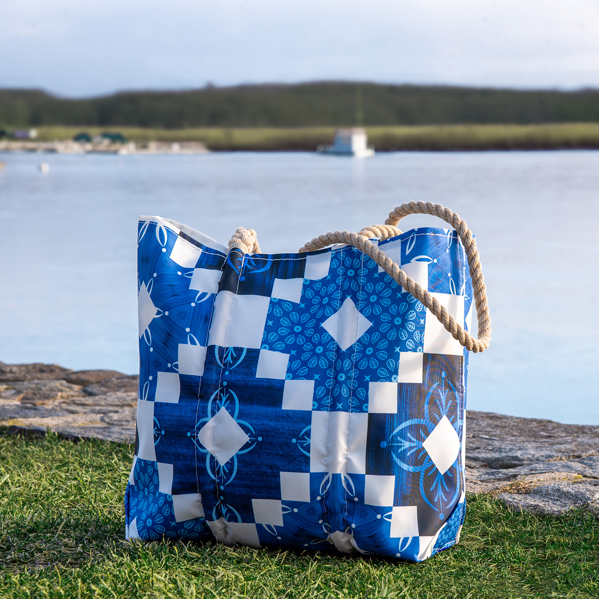 the indigo rising medium totes sits on a patch of grass by the ocean