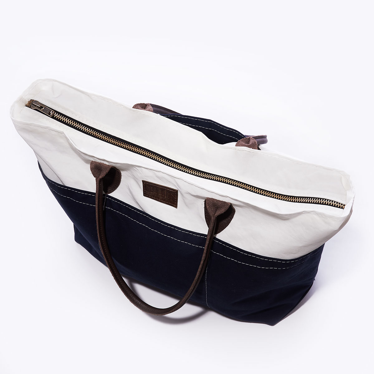 zippered closure of recycled sail cloth and navy canvas tote with rolled brown leather handles