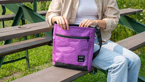 Woman sitting on bench holding a purple voyager bag